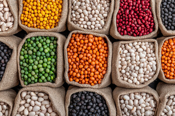 Fototapeta premium A vibrant assortment of colorful beans in burlap sacks, showcasing a diverse collection of legumes suitable for culinary and decorative uses.