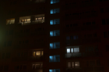 An enchanting nighttime view of an apartment building that beautifully showcases illuminated windows against a foggy urban environment, creating a captivating atmosphere of city life