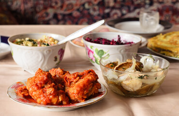 Stewed sea fish in tomato sauce in a plate on table in the foreground, two different salads and other dishes in the background, neat holiday table
