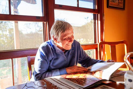 Senior woman reading cook book deciding what to bake sitting in home in winter sunshine