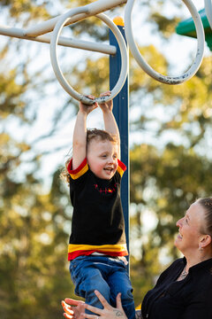 Happy Aboriginal toddler boy playing on monkey bar rings at park with mum