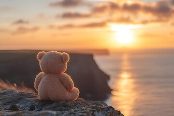 Back view of a teddy bear sitting on a stone and looking at the sea with a sunset sky in the background, Generative AI
