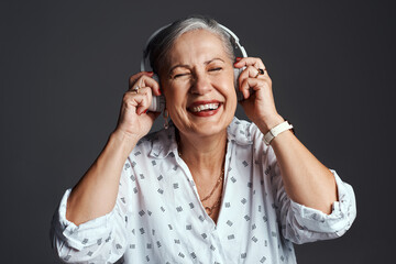 Happy, laugh and senior woman with headphones, funny and podcast in studio. Music, comedy audio and streaming radio with smile, joke and elderly style with grey background and listening to song