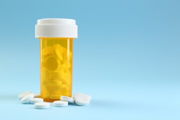 Bottle of antibiotic pills on light blue background, space for text