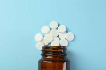 Bottle of antibiotic pills on light blue background, top view