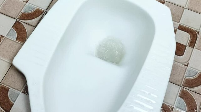 Flushing water in a white squat toilet using a green dipper in the bathroom