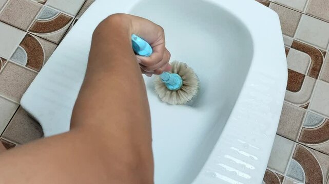 Cleaning the white squat toilet in the bathroom with a toilet brush