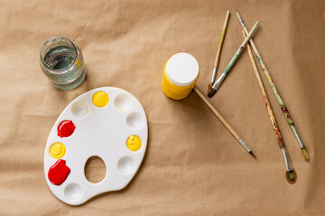 Art supplies arranged on table with paint palette, brushes, and water jar, at home