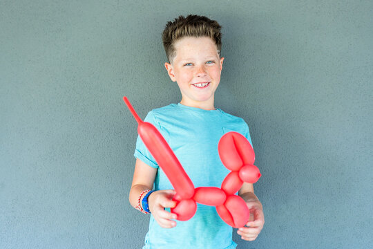 Boy with playful mischief holding a red balloon animal