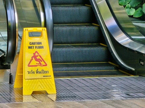 A caution wet floor sign displayed on an escalator, promoting safety awareness in a public space.