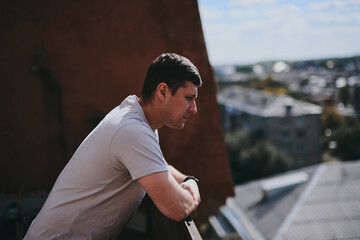 Fototapeta premium A thoughtful man stands on the balcony of a high-rise building and looks at the city panorama