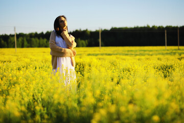 Fototapeta premium Pretty girl with a hat in her hand walks in a field with field flowers and smiles sincerely