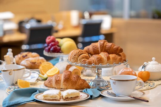 A delicious spread of croissants, pastries, fruits, and coffee, set up on a table in a modern office space, perfect for a corporate breakfast or a casual office party.