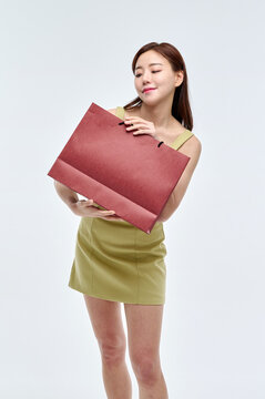 A beautiful Asian woman wearing a green one-piece dress and holding a red shopping bag in one hand stands in various poses.