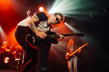 Guitarist performing energetically on stage with bandmates during live concert