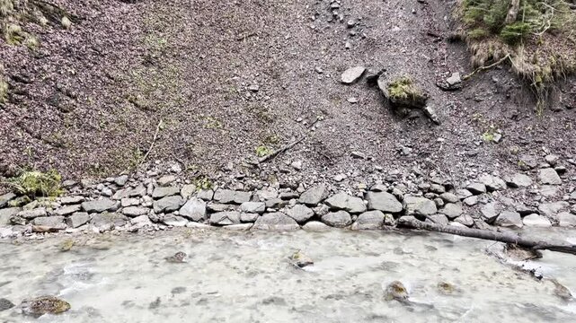 A tranquil river stream flows gracefully through the Partnach Gorge, nestled at the base of a majestic mountain. Captured on a misty day in Garmisch-Partenkirchen, Germany.