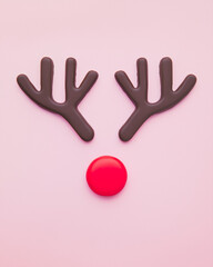 Obraz premium Flat lay of reindeer made of chocolate antlers and a red candy like nose on a light pink background. Minimal Christmas card with copy space 