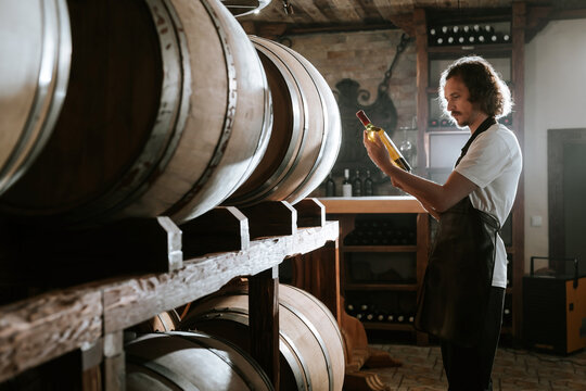 Winemaker Inspecting Bottle of White Wine in Cellar