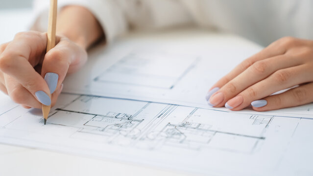 Closeup of professional caucasian female engineer hand drawing blueprint. Creative design and teamwork concept with blueprint and architectural equipments placed on table. Focus on hand. Immaculate.