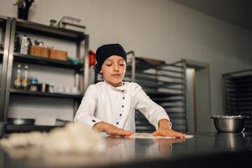 Fototapeta premium Young girl chef preparing dough in a professional kitchen setting.