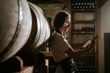 Winemaker Inspecting Bottle of White Wine in Cellar