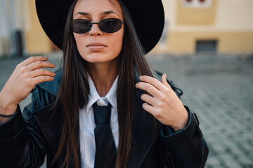Stylish woman wearing hat, sunglasses and tie posing outdoors