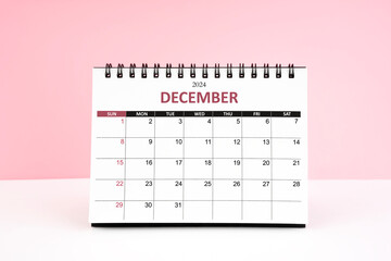 December 2024 desk calendar on white table with pink background.