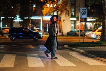Stylish woman crossing city street at night