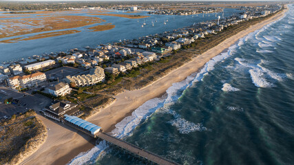 Coastal neighborhood at Wrightsville Beach, NC, seen from above, featuring rows of houses, a sandy beach, and blue waters with anchored boats in the inlet. © Red Lemon