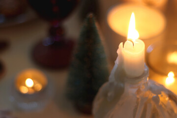 Various Christmas decorations, cookies, chocolate, nuts and tangerines, wine glasses and lit candles on the table. Holiday hygge at home. Selective focus.