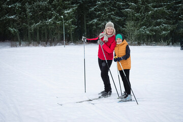 Happy family winter fun - child and grandmother skiing at snowy forest full length portrait