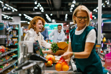 Cheerful customer passing groceries to cashier at checkout counter