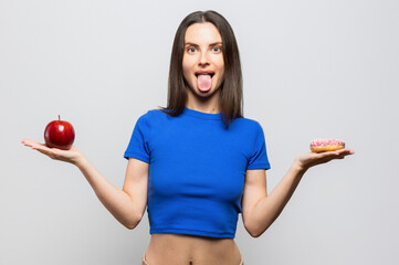 Beautiful young woman having to choose in between a donut and a red apple. On white background