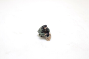 Miniature Figure Of A Person Sitting With Bag On White Surface