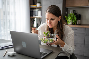 Tired woman eats food ordered at delivery service while sitting in her home office in front of laptop during lunch break. 