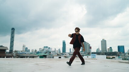 Motion shot of B-boy dance performance by professional street dancer at rooftop with sky scrapper, city view. Attractive asian hipster show energetic footstep. Outdoor sport 2024. Hiphop.