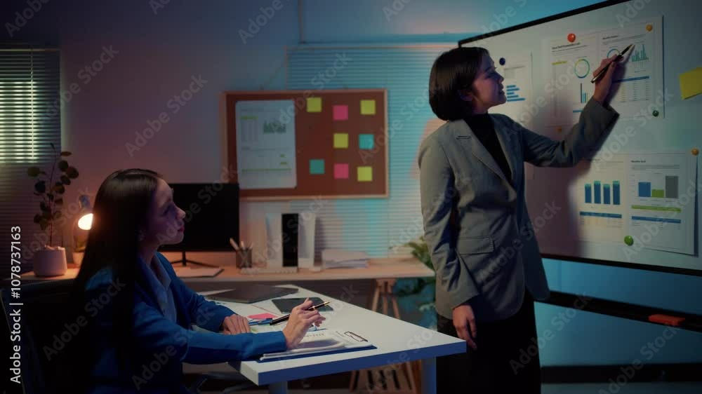 Poster businesswoman is using a whiteboard to explain a strategy to her colleague. the colleague is sitting