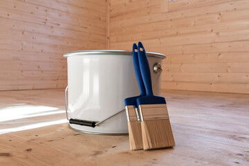 A paint can and brushes on a wooden floor, with wooden walls in the background, illustrating wood surface protection and maintenance