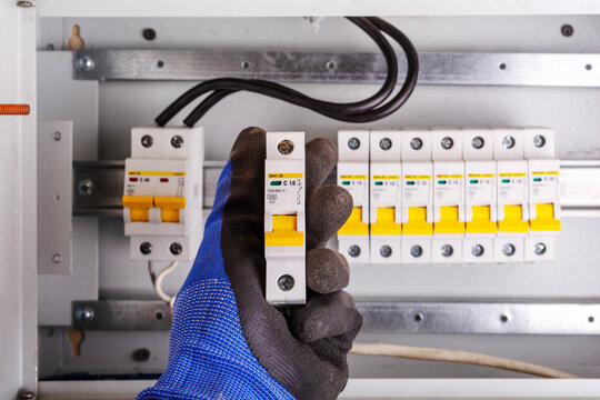 Electrician in blue glove holding circuit breaker in front of row of switches in distribution box