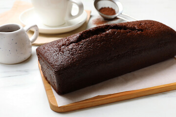 Tasty chocolate sponge cake and ingredients on white marble table, closeup