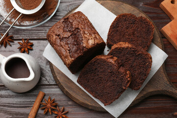 Delicious cut chocolate sponge cake and ingredients on wooden table, flat lay