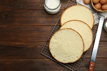 Delicious cut sponge cake, knife and ingredients on wooden table, flat lay. Space for text