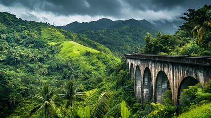 A stone bridge arches over a lush valley, with palm trees and green hills in the distance, under a cloudy sky.