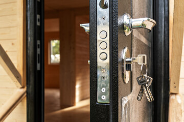 Open door with keys in lock against new wooden house background, concept of readiness for moving in