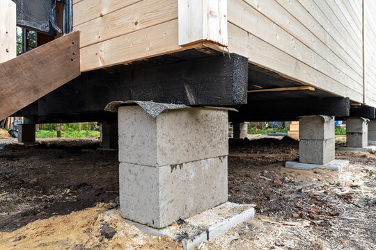Foundation on concrete blocks for a wooden frame house, providing structural stability with black waterproofing on the wooden frame