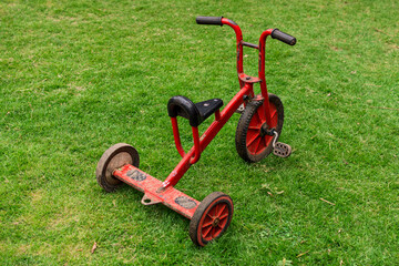 Old red tricycle with a worn look standing on green grass, evoking memories of outdoor childhood play