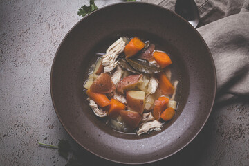 Chicken soup with potatoes and carrots in brown plate, dark background. Comfort food concept.