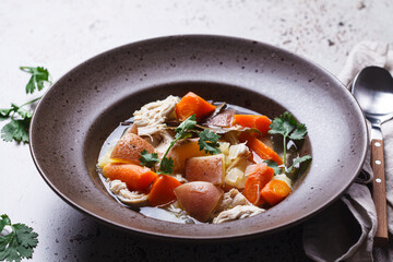 Chicken soup with potatoes and carrots in brown plate, dark background. Comfort food concept.