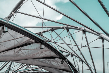Metal structures with mesh and cables under a blue sky, forming an abstract modern architectural design