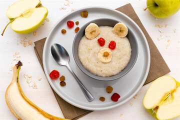 Funny kids childrens baby's healthy breakfast lunch oatmeal porridge like bear face with apple,banana,fruits. dessert food art on white wooden table